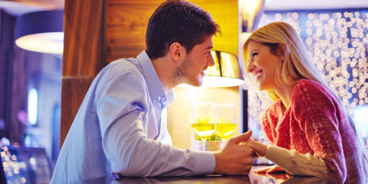 Frau und Mann um die 30 bei romantischem Treffen in einer Bar. Sie schauen sich verliebt an und er hält ihre Hände über den Tisch hinweg