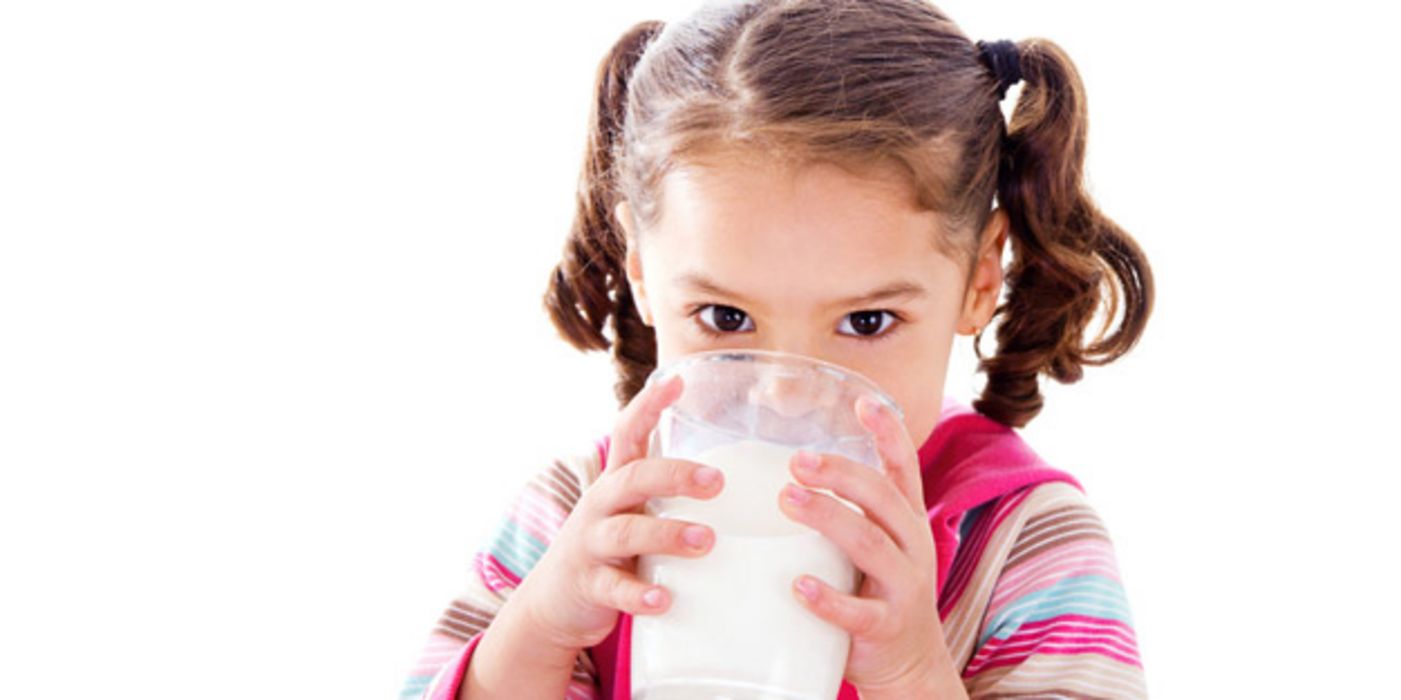 Kleines Mädchen trinkt Milch aus einem großen Glas