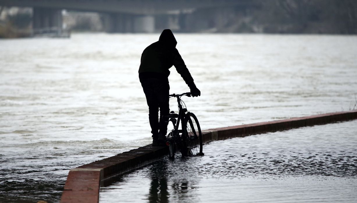 Mann, schiebt sein Fahrrad durch überflutete Straßen.