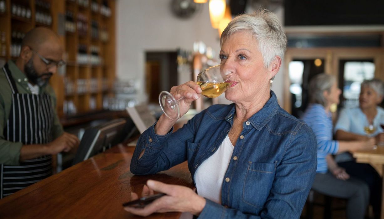 Ältere Frau, trinkt ein Glas Wein.