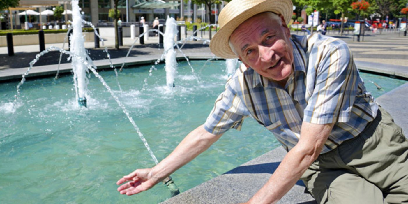 Sommerszene: Senior mit Strohhut an Stadtbrunnen in Bratislava, am Rand sitzend, eine Hand im Wasser
