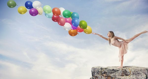 Tänzerin in der Waage stehend auf einem Felsvorsprung stößt mit ausgestrecktem Zeigefinger eine Traube Luftballons über dem Abgrund an