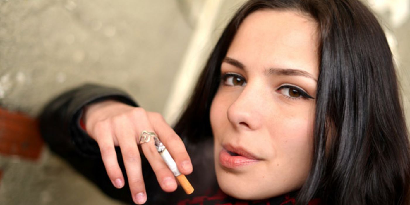 Portrait junge dunkelhaarige Frau schaut in die Kamera und raucht