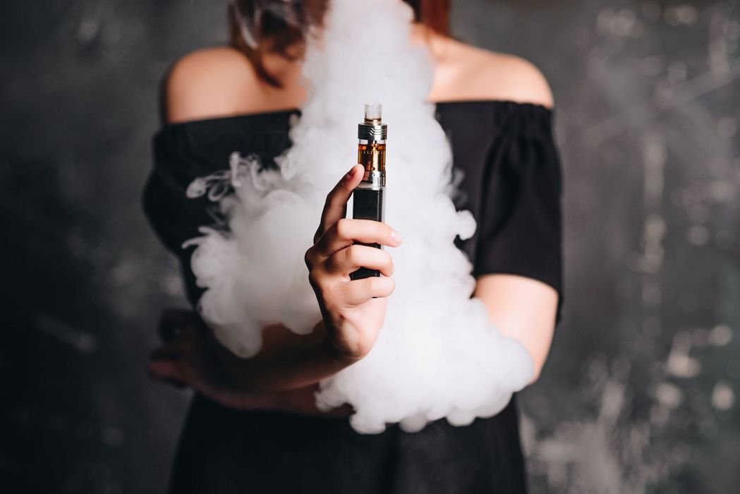 Frau mit einer E-Zigarette, umgeben von Dampf.