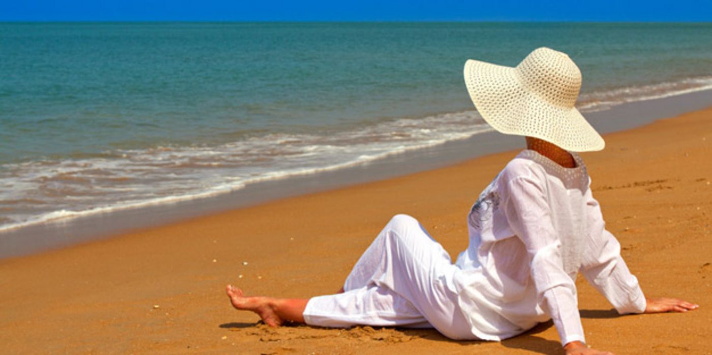 Weiß gekleidete Frau mit weißem Sonnenhut an exotischem Strand
