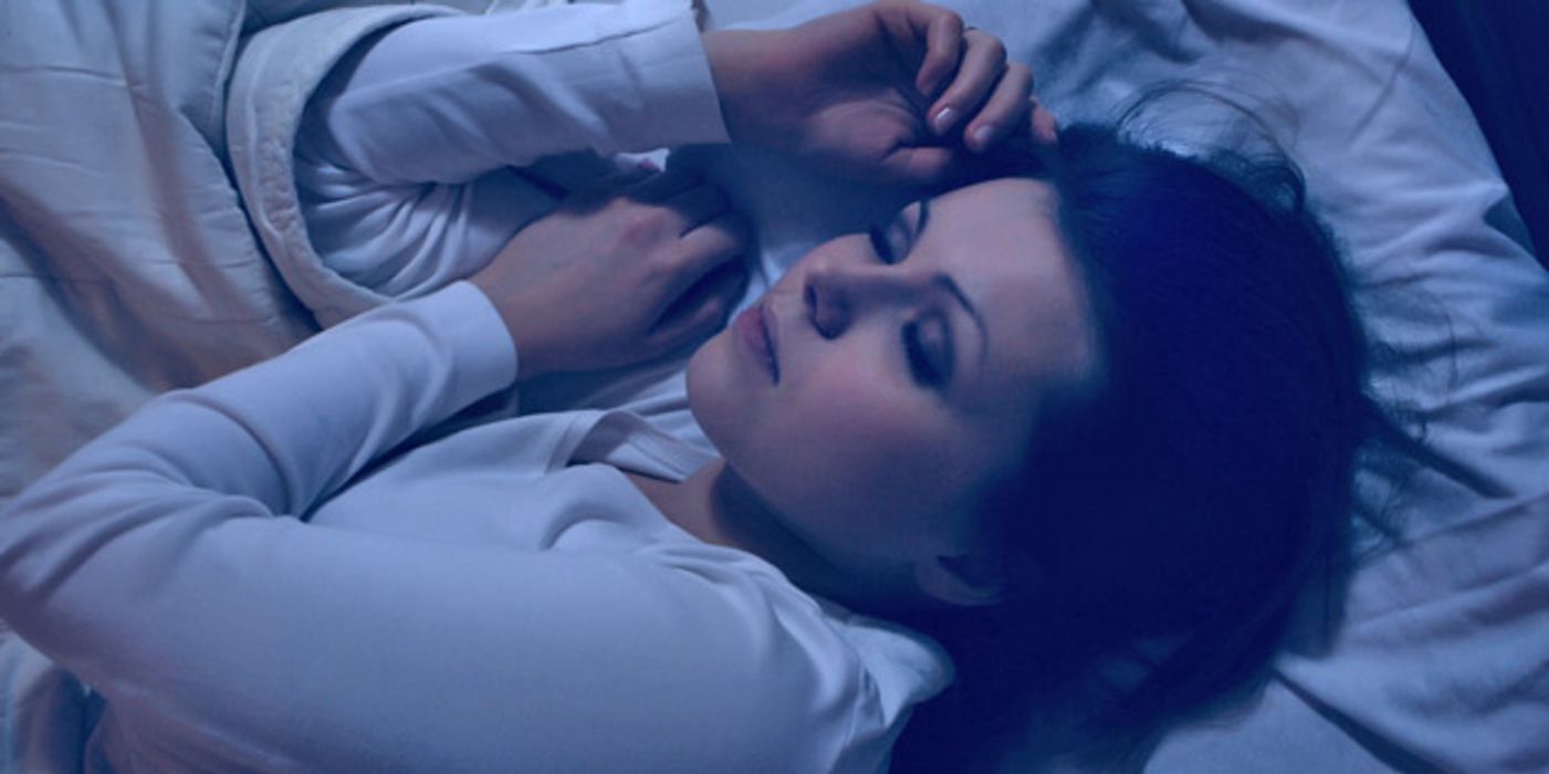 Nahaufnahme Oberkörper Frau ca. Ende 20, dunkelhaarig, weißer Schlafanzug, beim Schlafen in Dunkelheit im Bett