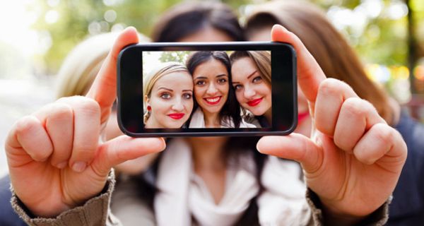 Drei Teenager-Mädchen stecken die Köpfe zusammen und machen ein Handyfoto von sich