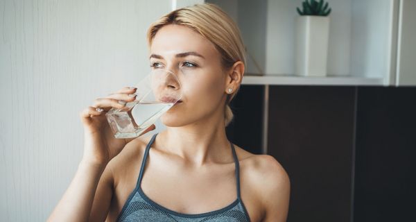 Junge blonde Frau, trinkt ein Glas Wasser.