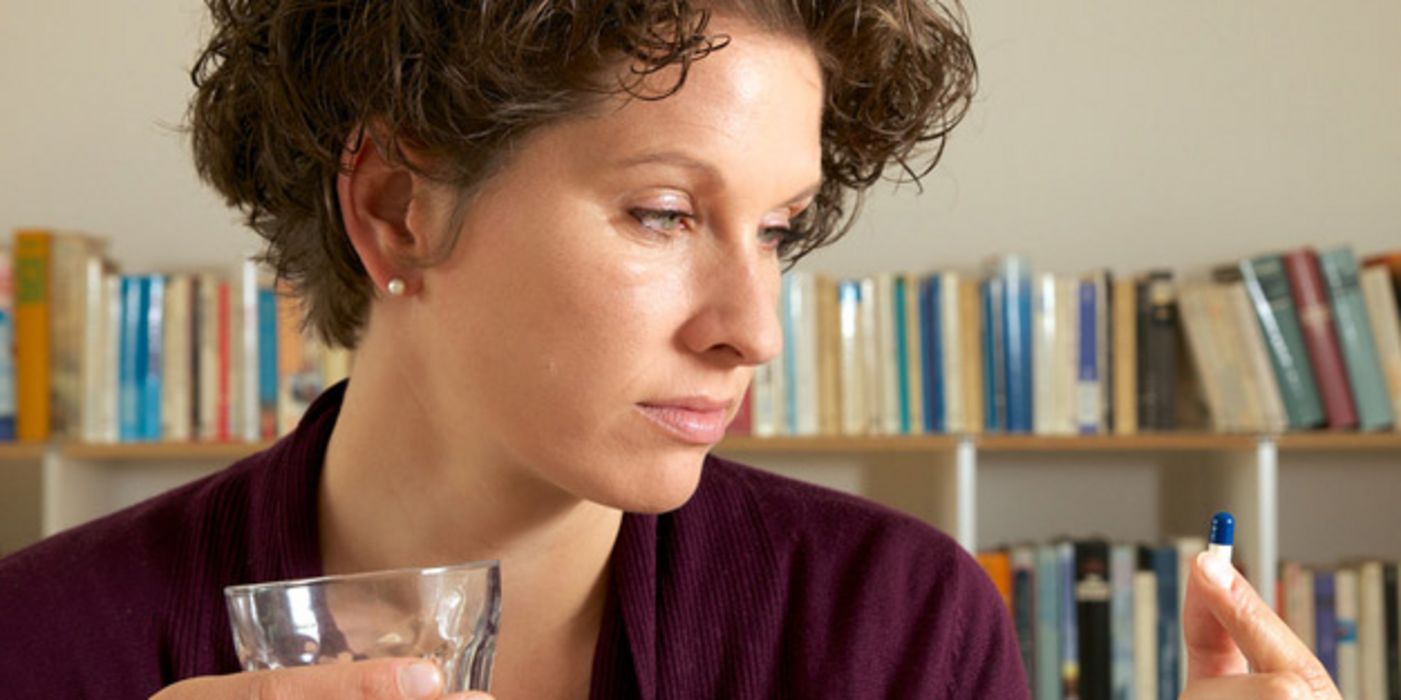 Frau schaut skeptisch auf Kapsel, die sie gerade mit einem Glas Wasser einnehmen will