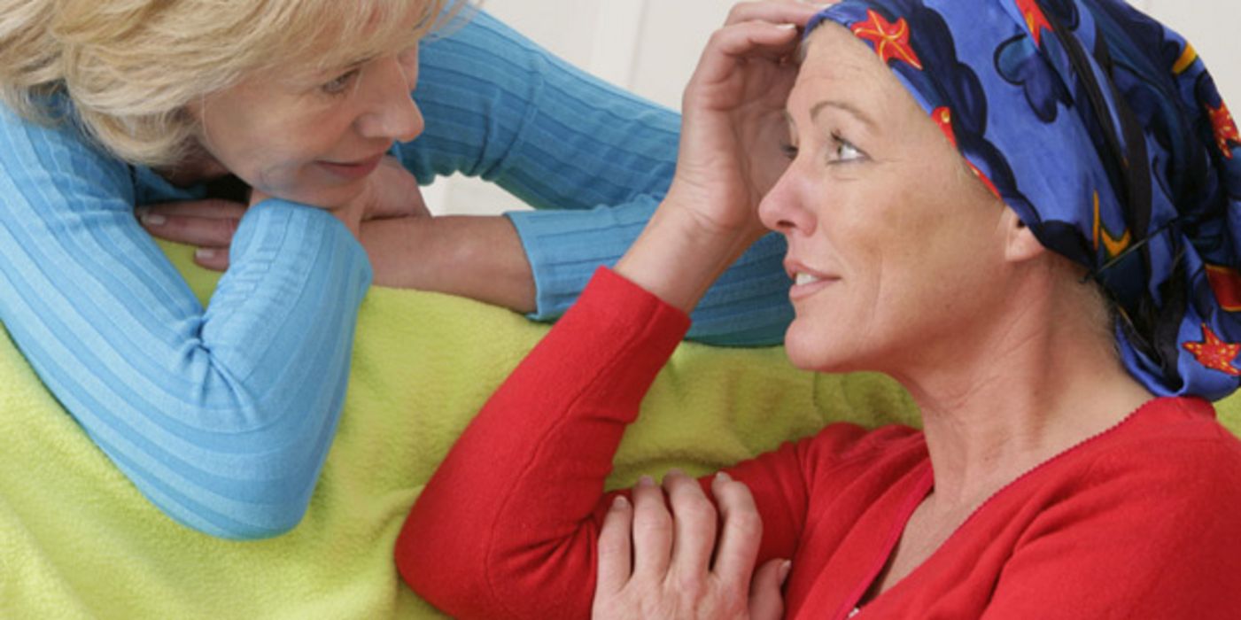 Brustkrebspatientin ca. Mitte, Ende 40, blaugemustertes Kopftuch, roter Pulli, im Gespräch mit blonder Frau um die 50, blond, helllauer Pulli