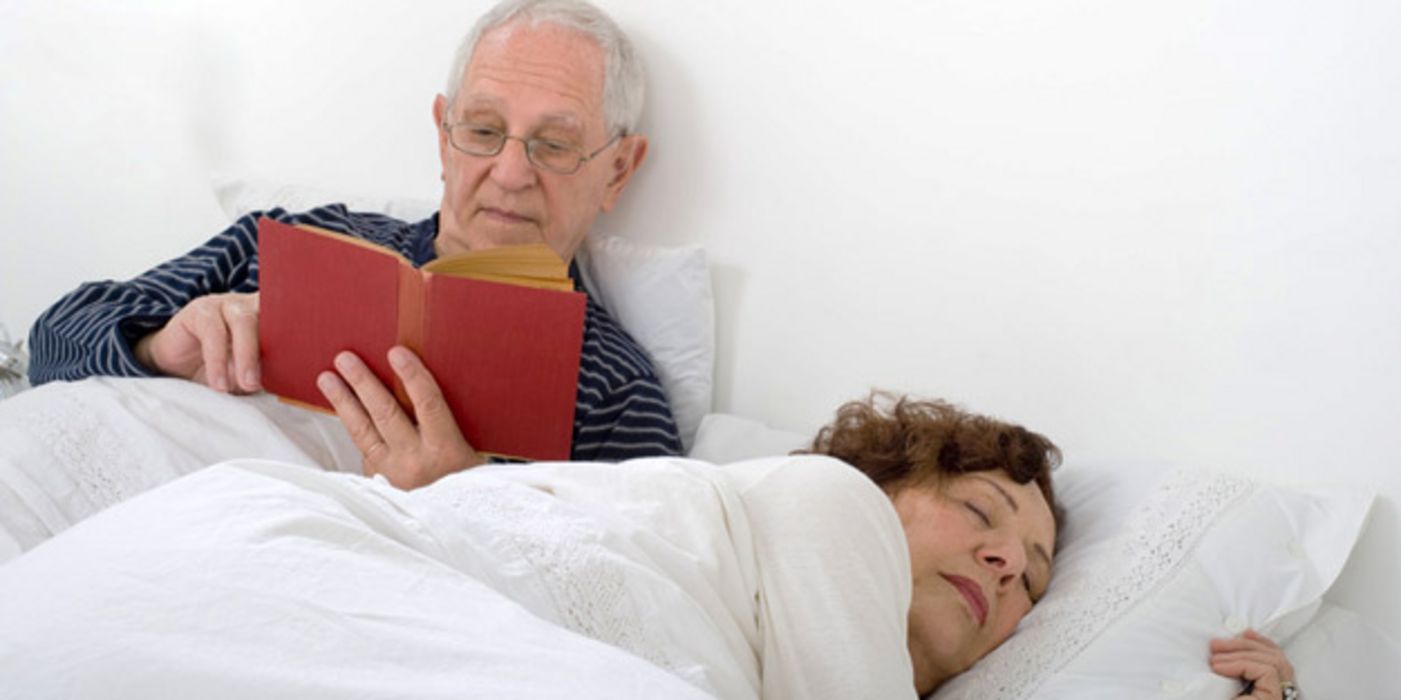 Paar im Bett, Mann (ca. 70) liest, Frau (ca. 60er) schläft