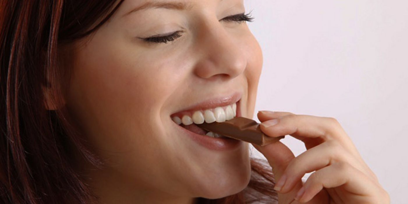 Frau beißt in einen Riegel Schokolade.