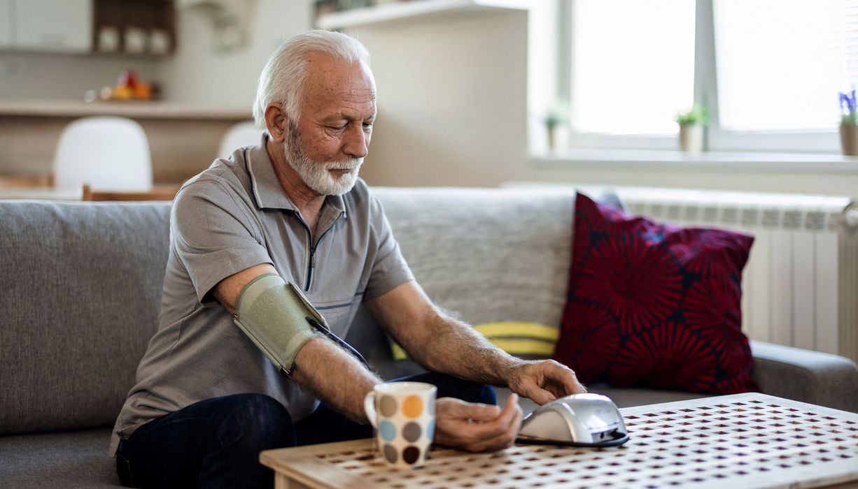 Älterer Mann, bedient ein Blutdruckmessgerät.