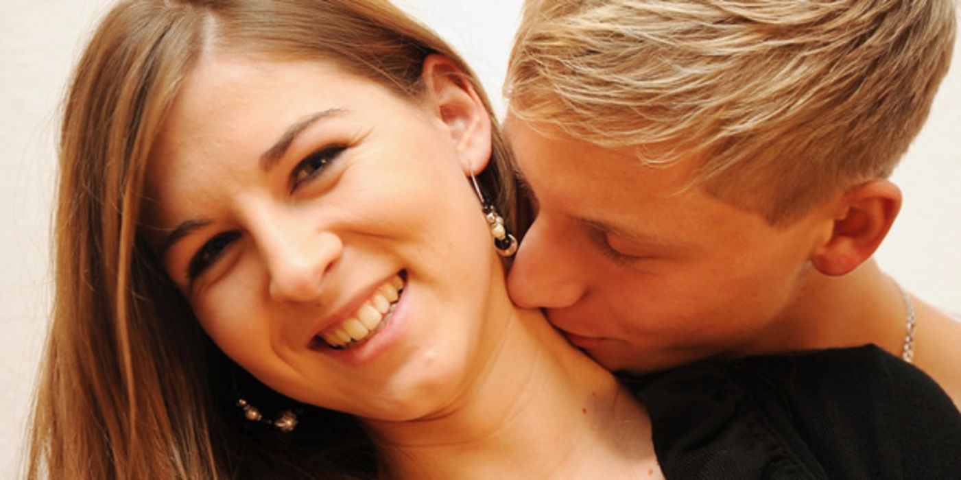 Junger Mann küsst attraktive Partnerin auf den Hals.