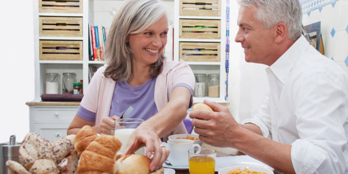 Älteres Paar beim Frühstücken, sie greift nach einem Brötchen in einem Brotkorb