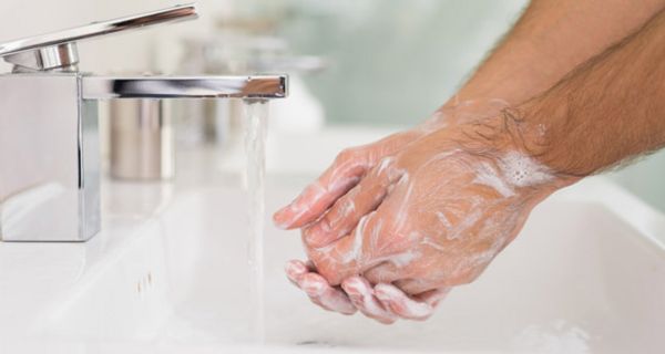 Eingeseifte Männerhände über Waschbecken unter fließendem Wasserhahn