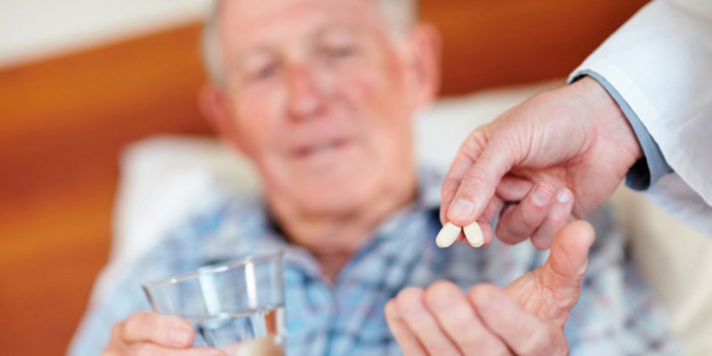 Alter Mann bekommt von einem Arzt zwei Tabletten in die Hand gedrückt