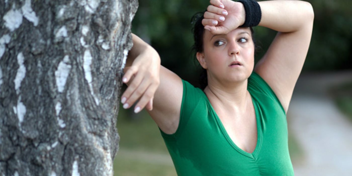 Junge Frau lehnt außer Atem vom Joggen an einem Baum