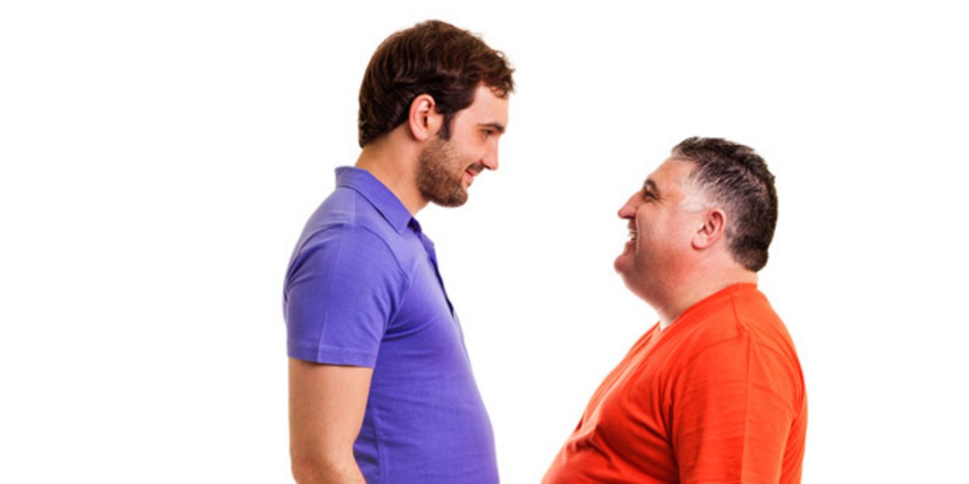 Großer, junger, schlanker Mann in blauem T-Shirt und kleiner, dicker, älterer Mann in rotem T-Shirt stehen sich gegenüber