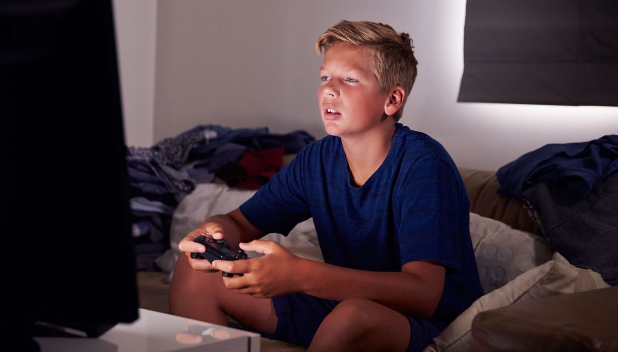 Junge mit Spielkonsole in der Hand starrt auf seinen Fernseher