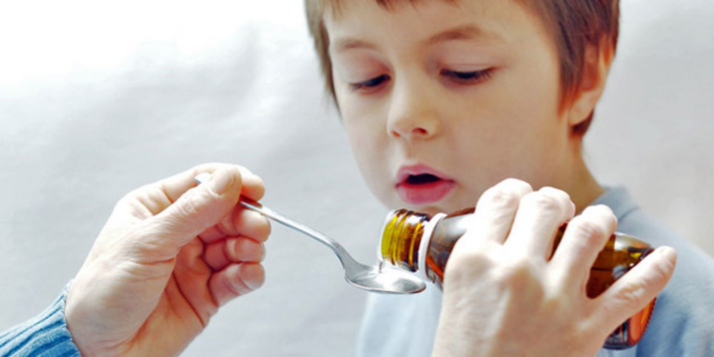 Junge, ca. 6 Jahre alt, bekommt mit einem Löffel aus einer Medizinflasche ein Medikament