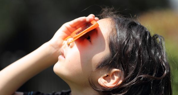 Kind, schaut durch eine spezielle Brille in die Sonne.