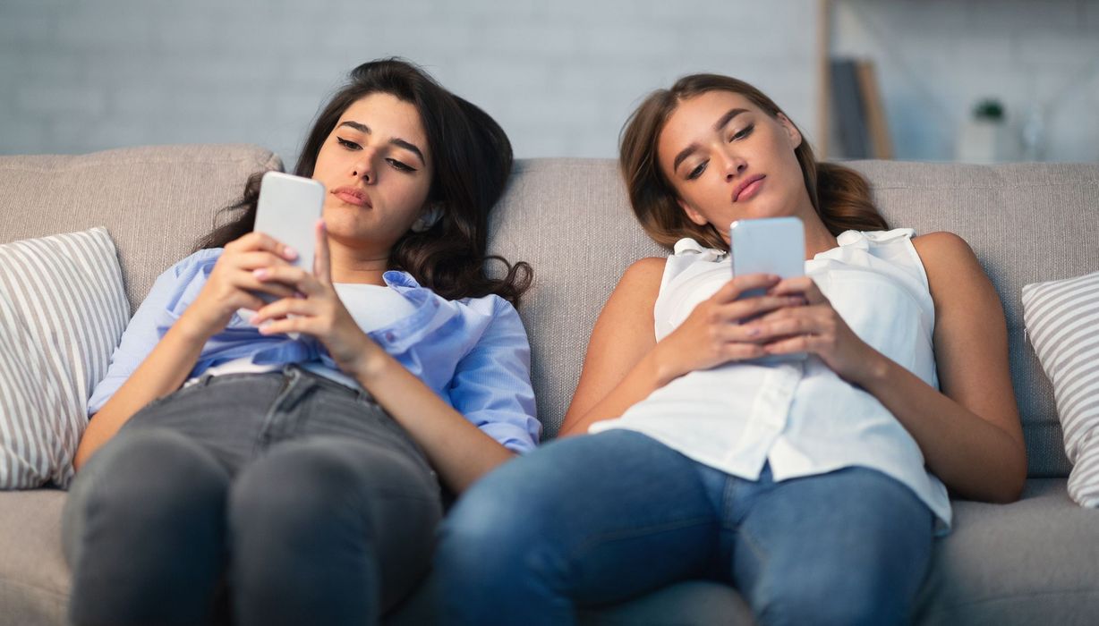 Zwei jugendliche Mädchen, liegen mit ihren Smartphones auf der Couch.