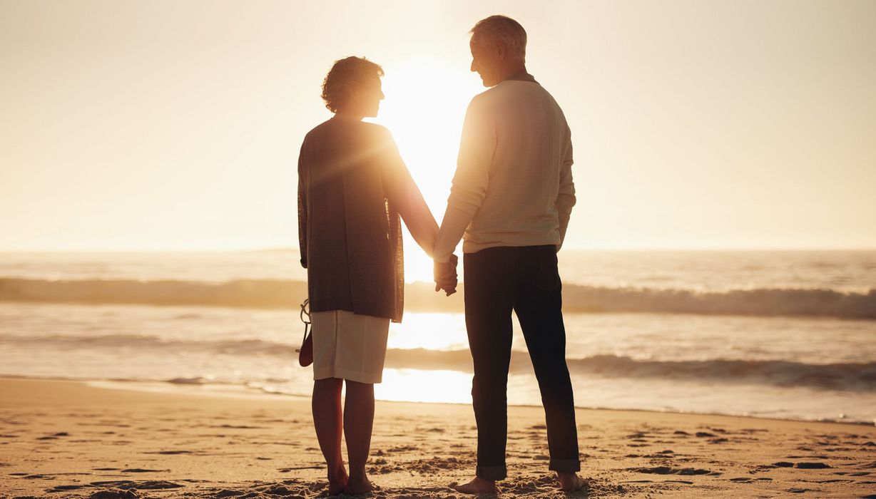 Paar, steht am Strand und hält sich an der Hand.