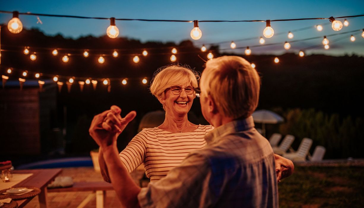 Ein älteres Paar, tanzt abends unter einer Lichterkette.