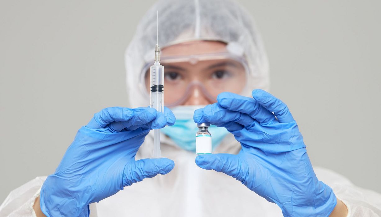 Forscher hält Impfstoff und Nadel in beiden Händen.