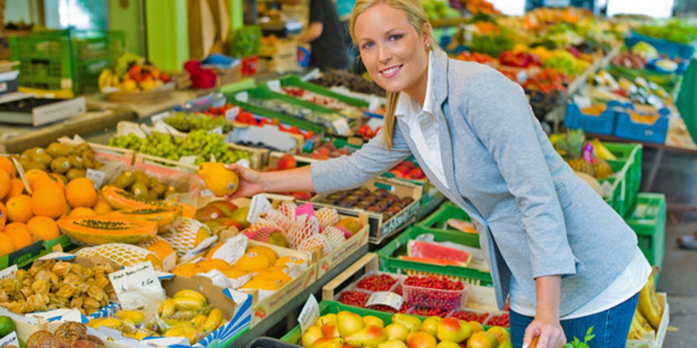 Frau an einem Marktstand mit Obst und Gemüse
