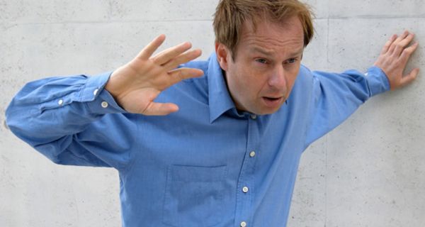 Mittelalter Mann im blauen Hemd stützt sich an einer Wand ab, weil ihm schwindelig ist