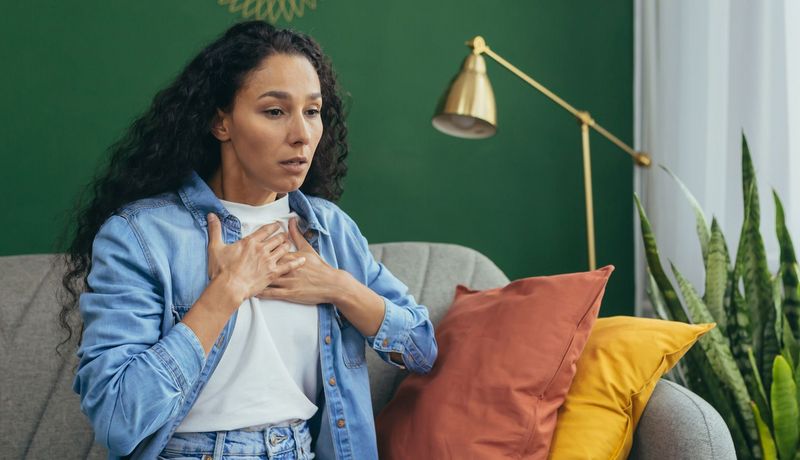 Frau ringt um Luft und presst sich beide Hände auf das Brustbein.