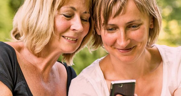 Zwei Frauen in der Natur schauen auf ein Smartphone