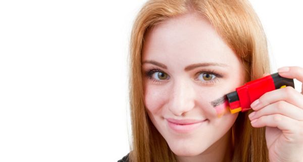Jugendliche schminkt sich mit Schminkstift eine Deutschlandflagge auf die Wange