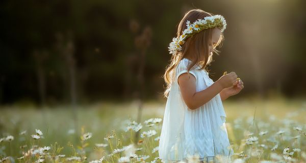 Junges Mädchen steht in einer Blumenwiese und betrachtet eine Blume.