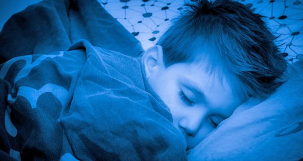Blaugetöntes Foto (Nacht) eines ca. 9 jährigen schlafenden Jungen, Bettdecke bis zum Kinn hochgezogen