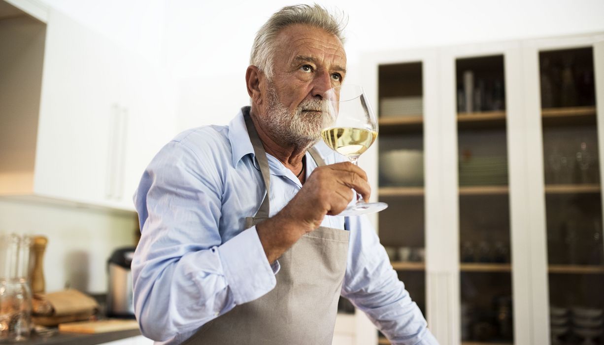 Grauhaariger Mann trinkt ein Glas Weißwein.