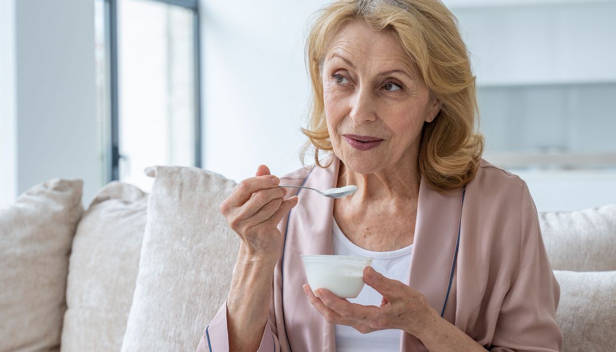 Ältere Frau, isst einen Becher Joghurt.