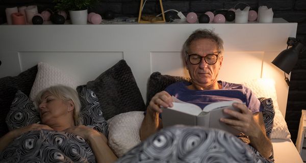 Senioren-Paar liegt im Bett, Mann ist noch wach und liest.