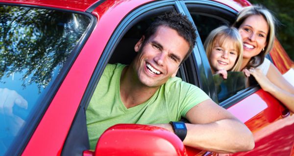 Vater, Mutter, Kind lehnen sich aus einem roten Auto