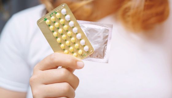 Frau, hält eine Pille und ein Kondom in der Hand.