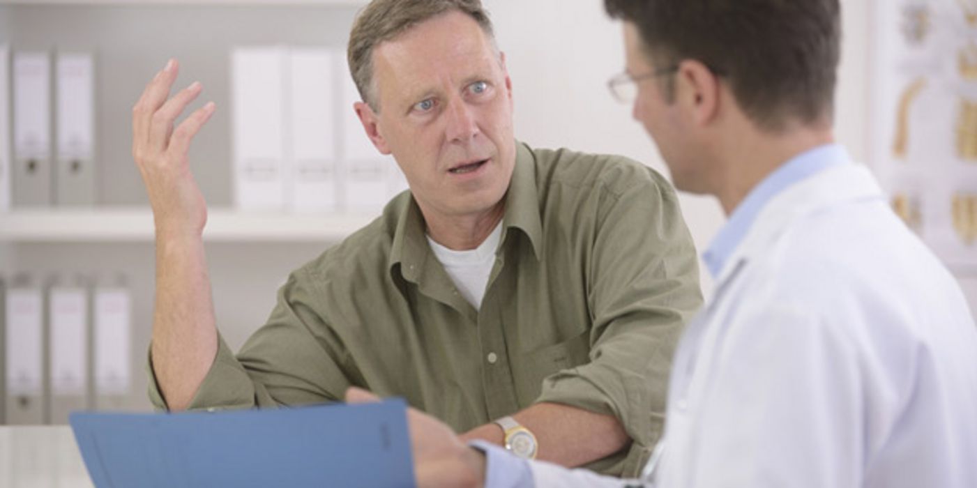 Mann in mittleren Jahren im grünen Hemd spricht mit einem Arzt in der Praxis