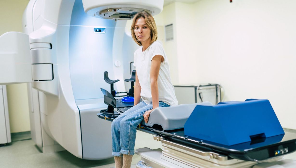 Junge Frau sitzt auf der Liege eines Bestrahlungsgeräts.