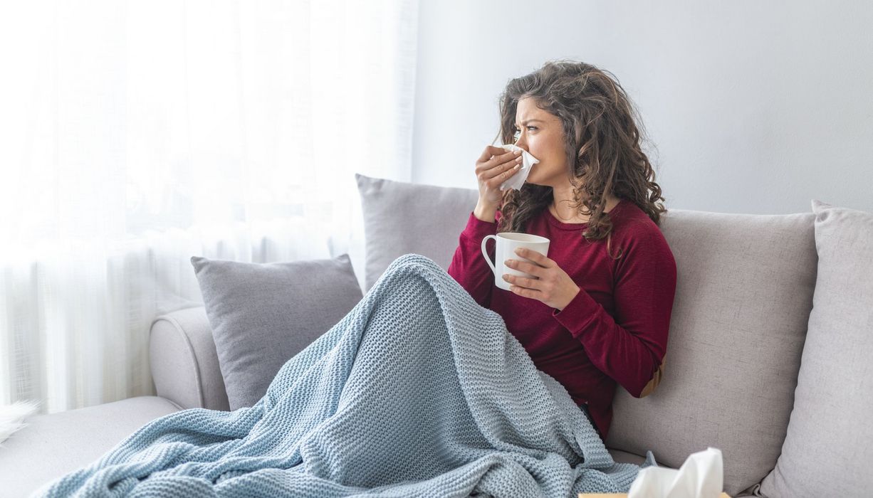 Frau mit Erkältung sitzt auf dem Sofa und putzt sich die Nase