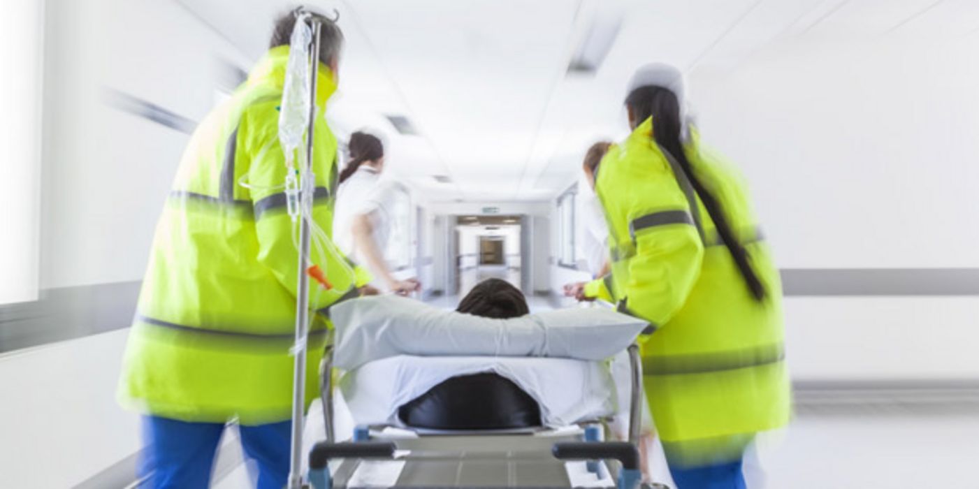 Einlieferung eines Notfalls ins Krankenhaus, Liege und Notfallpersonal, von hinten fotografiert, rechts und links neben Liege, Oberkopf von Patient zu sehen