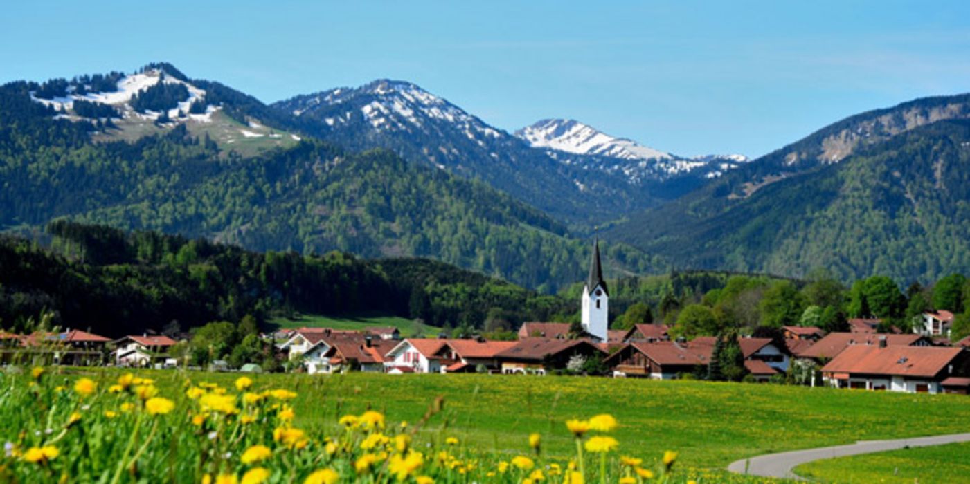 Blick auf ein Dorf im Voralpenland mit Kirchturm und Blumenwiesen
