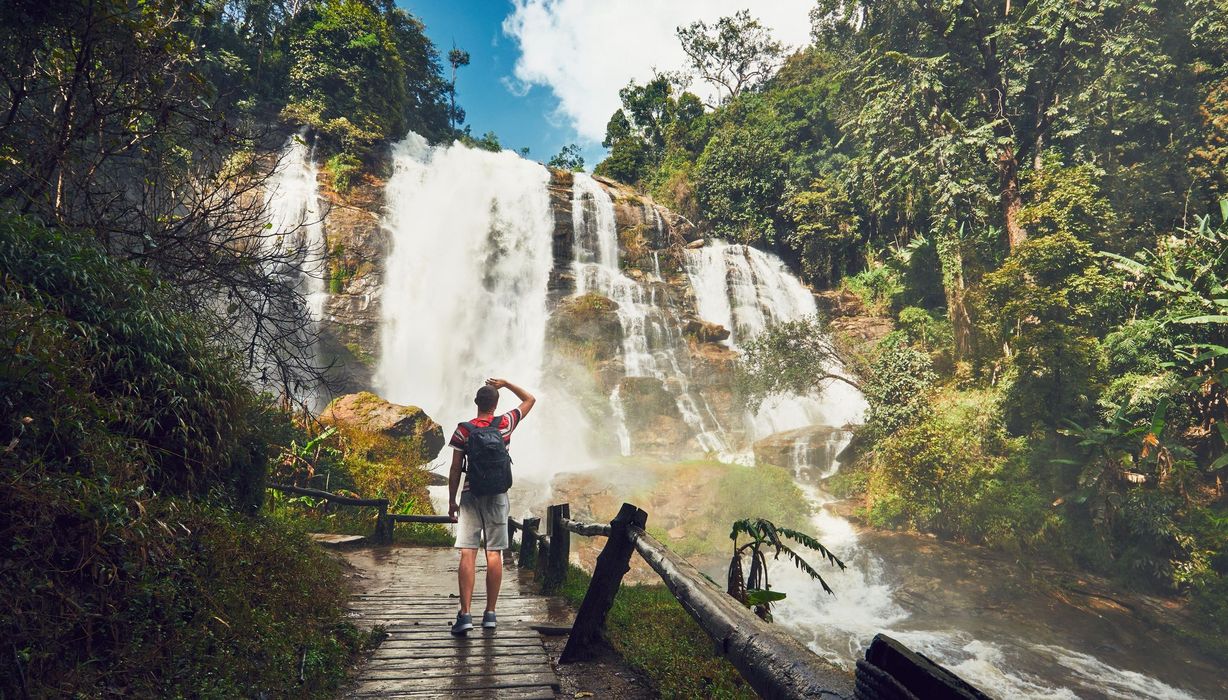 Mann mit Rucksack, steht vor einem großen Wasserfall.