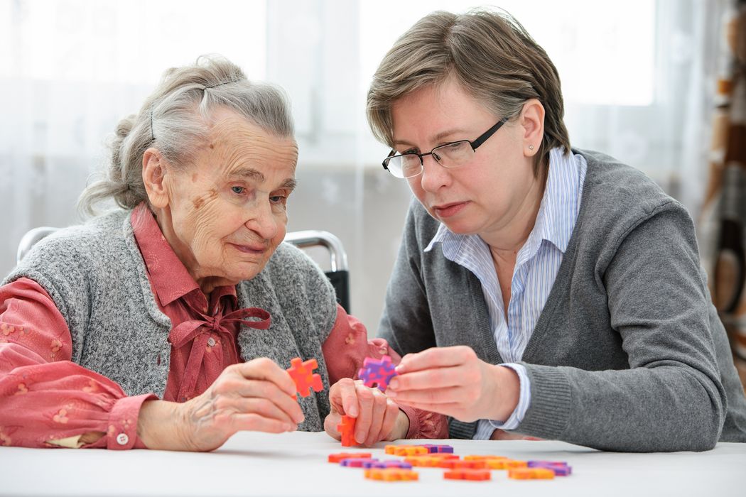 Ältere Frau löst ein Puzzle mit Pflegerin.