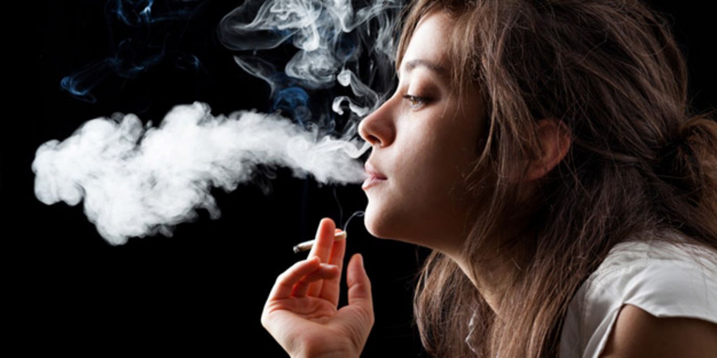 Profilansicht junger Frau in weißer Sommerbluse, Zigarette in der Hand, eine große Rauchwolke ausstoßend